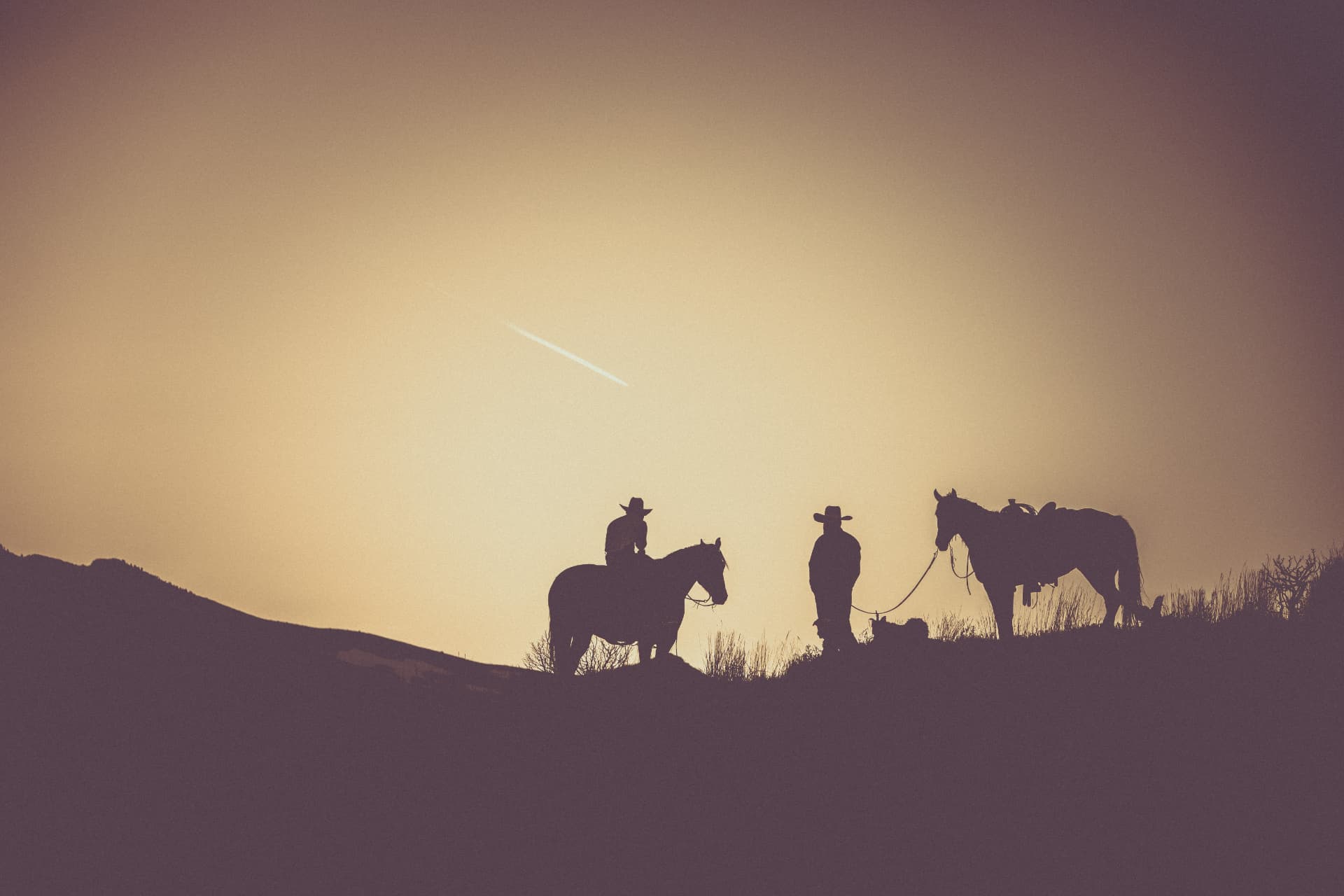Two riders resting on a ridge silhouetted against a warm evening sky